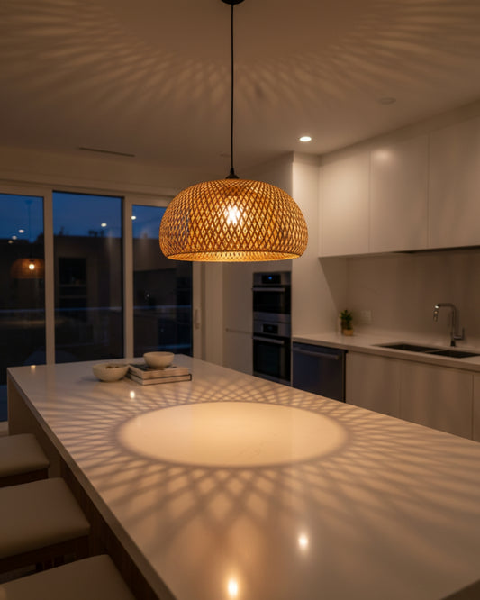 Handwoven bamboo dome pendant light over a kitchen island, lamp on at 2700K; straight black cord and canopy. Warm halo with lattice shadow pattern spreads on the countertop and ceiling in a Japandi/Scandinavian setting.