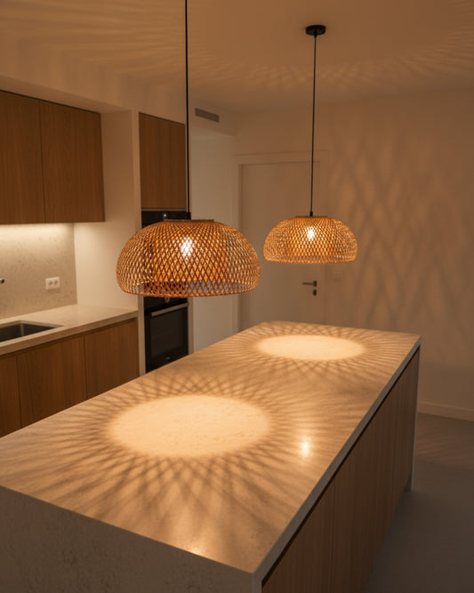 Two handwoven bamboo dome pendant lights over a kitchen island, lamps on at 2700K. Straight black cords and round canopies; warm halos with crisp lattice shadows on the countertop and ceiling in a minimalist Scandinavian kitchen.