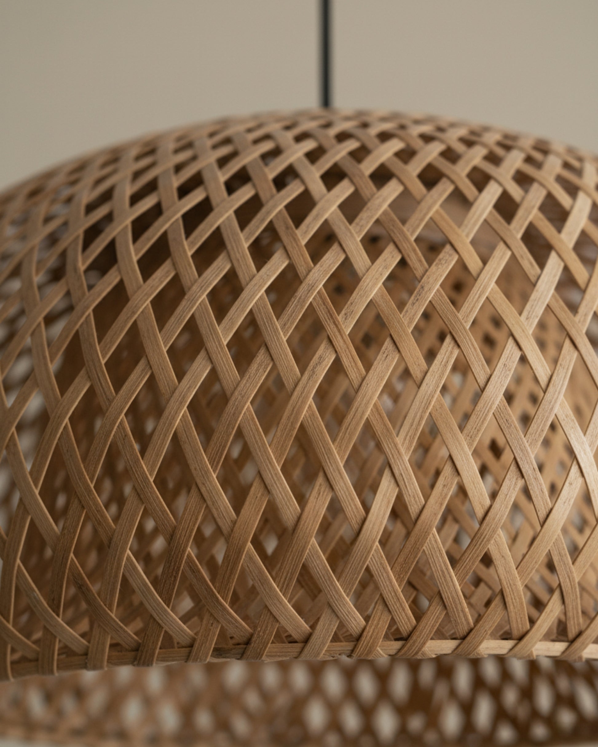 Close-up of a handwoven bamboo dome lampshade showing the diamond lattice pattern and rim detail; natural honey-brown fibers with subtle grain, soft studio lighting, black suspension cord slightly visible above.
