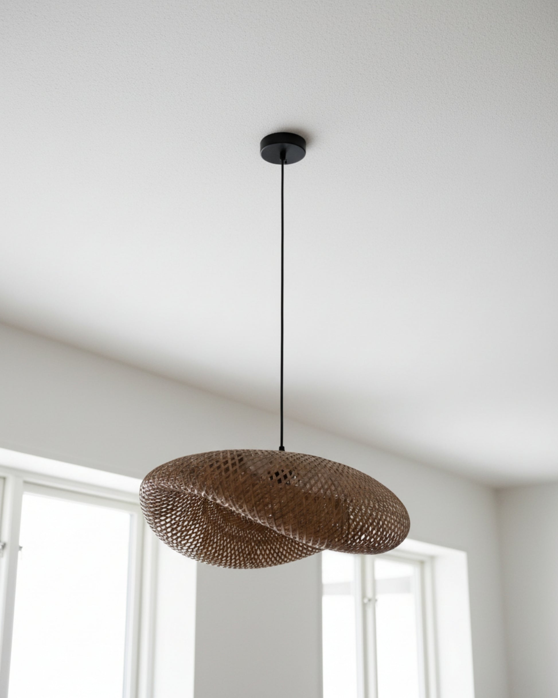 Eye-level daylight view of a handwoven bamboo twisted-disc pendant, black canopy and slim cord, lamp OFF; approx. 31.5 in (80 cm) diameter; natural rattan tone; ideal over kitchen islands or dining tables in Japandi/Scandinavian interiors.