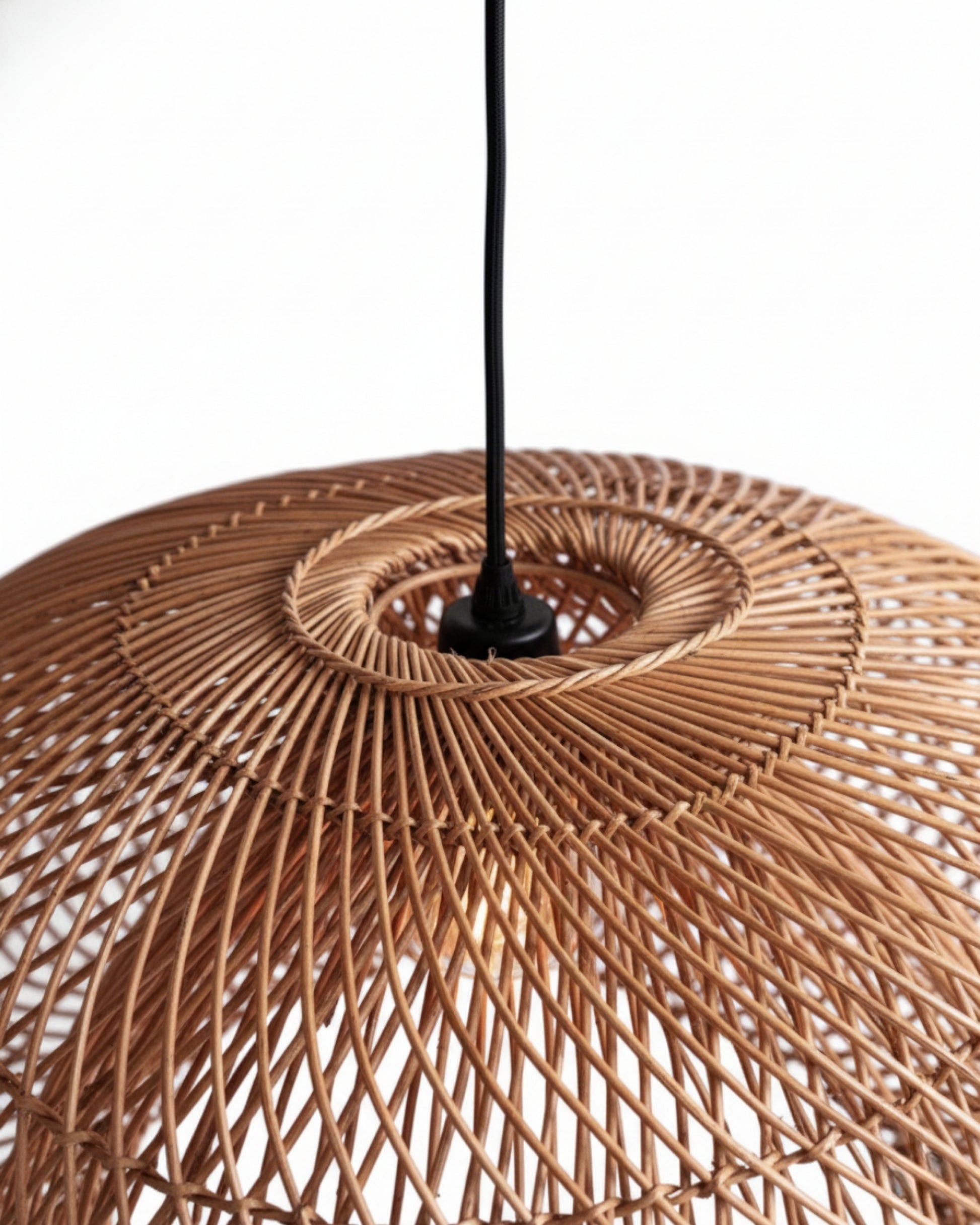 Close-up of a handwoven rattan pendant shade showing the spiral lattice and central ring with black cord; natural honey-brown finish and airy weave that casts patterned light—ideal for Japandi/Scandi interiors.