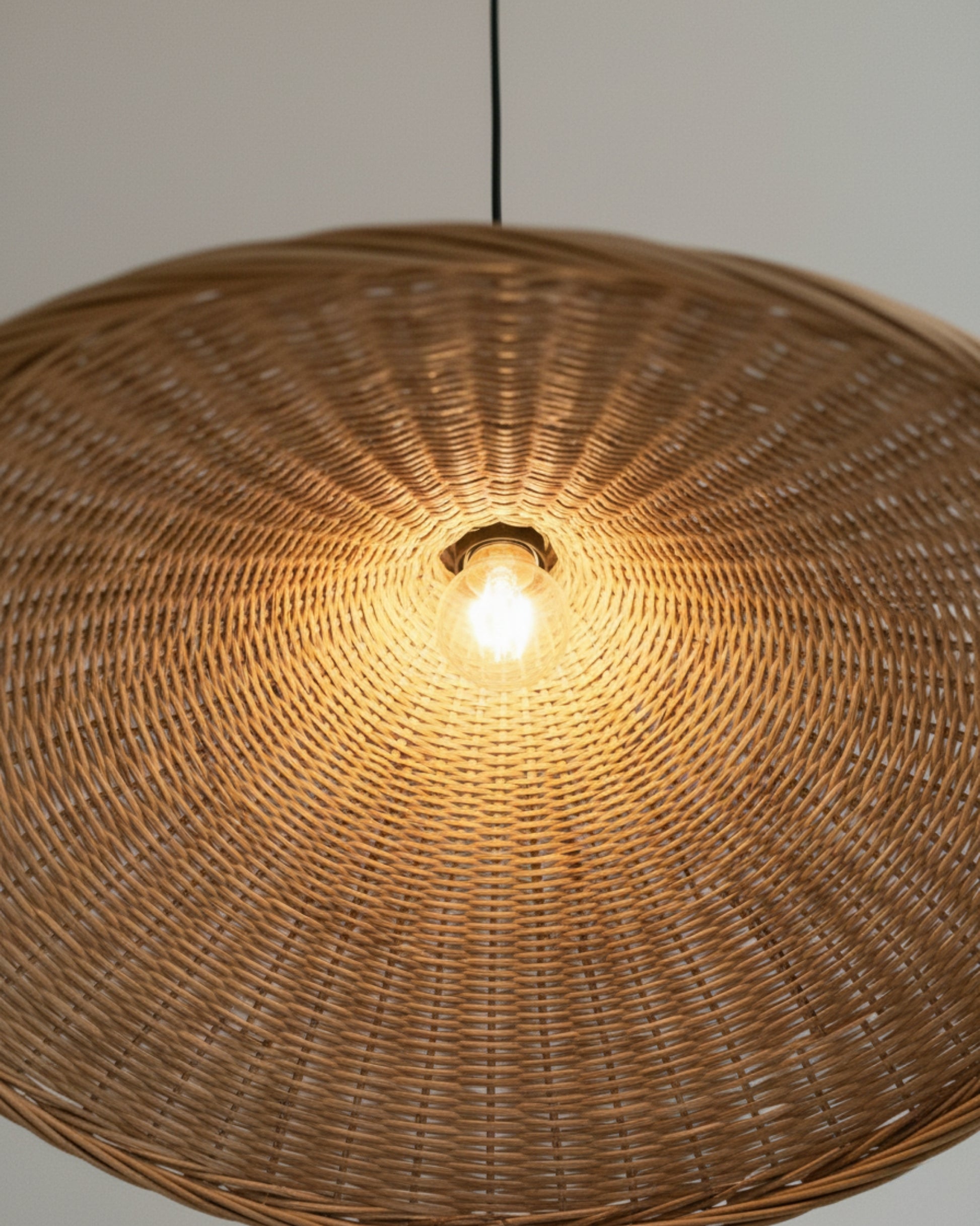 Close-up of a handwoven rattan pendant light with a sculptural wave shade; warm 2700K glow and visible E27 bulb show the radial weave detail—ideal above a kitchen island or dining table.