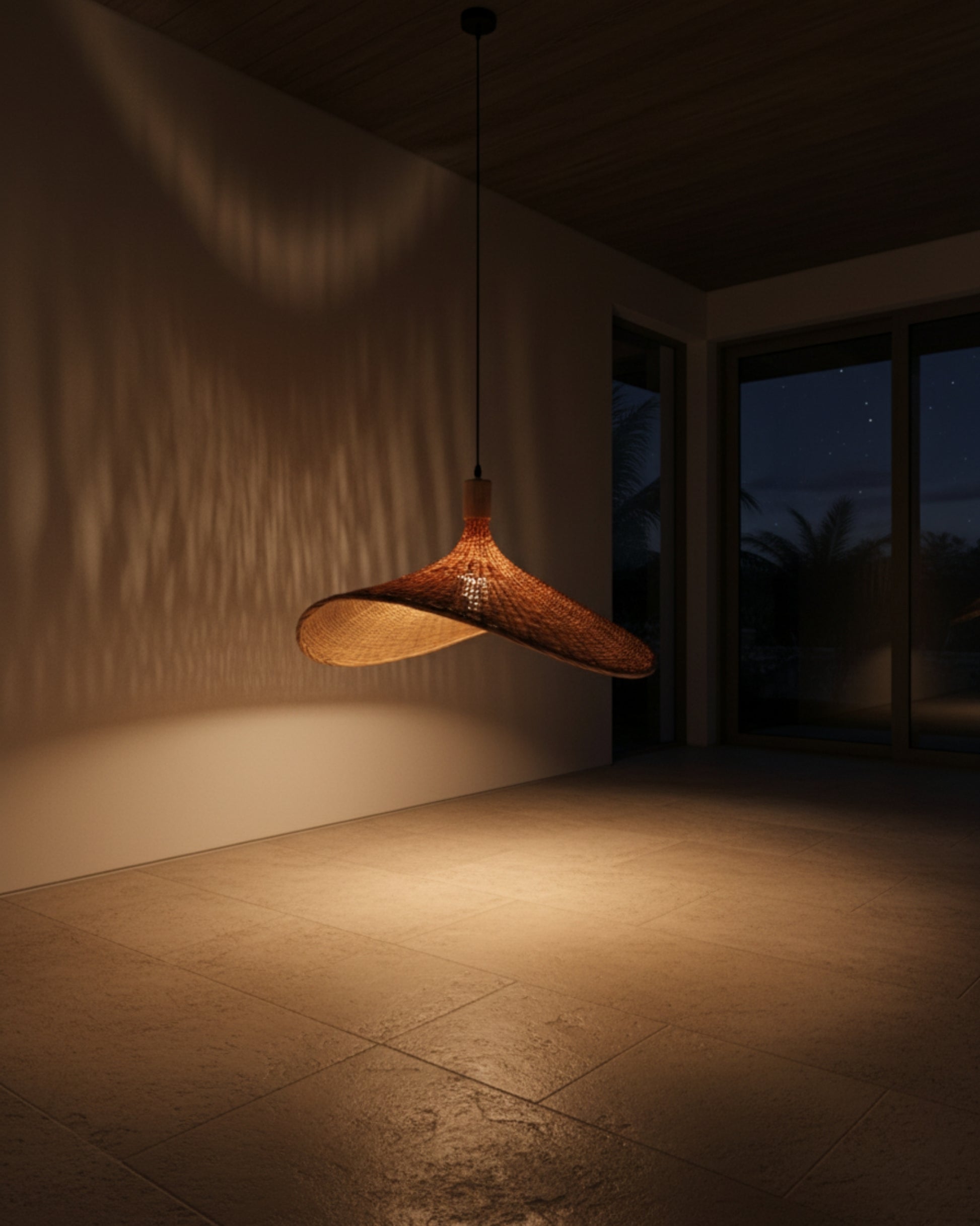 Night view of a handwoven rattan pendant with a sculptural wave shade; lamp on at 2700K casts a warm pool on the floor and dappled wall shadows; hangs from a black cord—ideal over a dining table or kitchen island.
