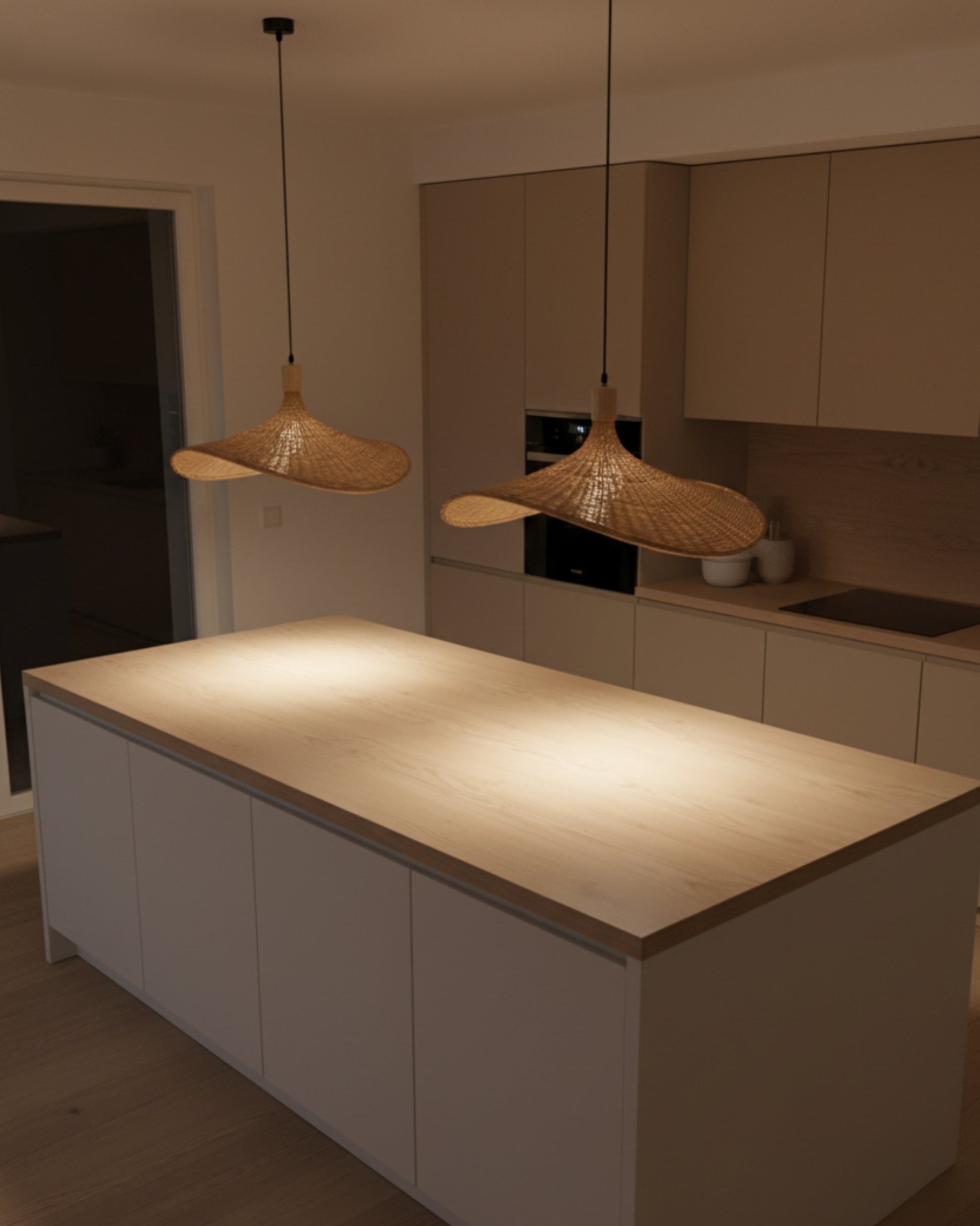 Pair of handwoven rattan pendant lights with sculptural wave shades over a kitchen island; warm 2700K pools on the countertop; adjustable drop, E27 LED compatible—Japandi style.