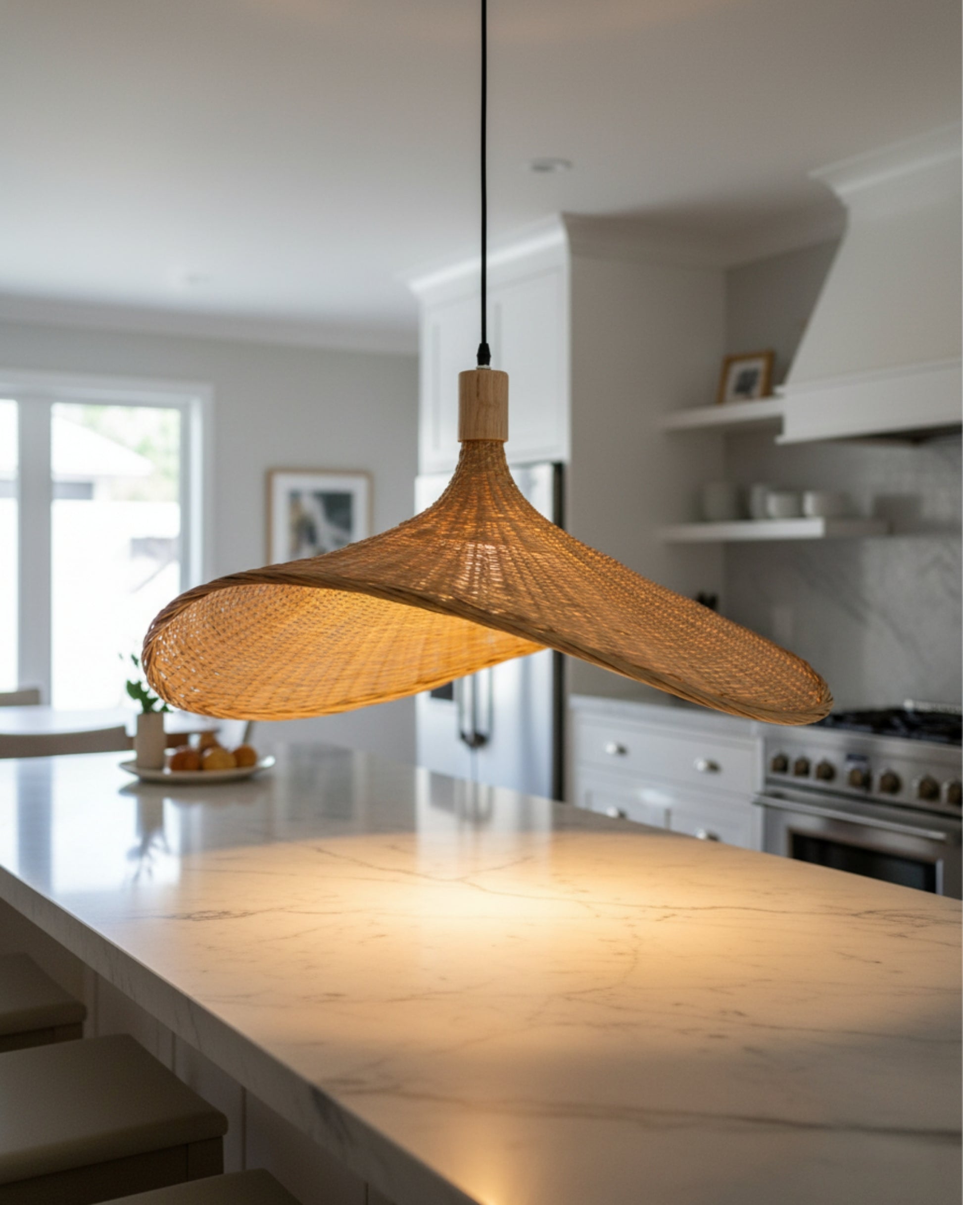 Handwoven rattan pendant light with a sculptural wave shade over a marble kitchen island; warm 2700K pool on the countertop, wood cap with black cord; E27 LED compatible with adjustable drop.
