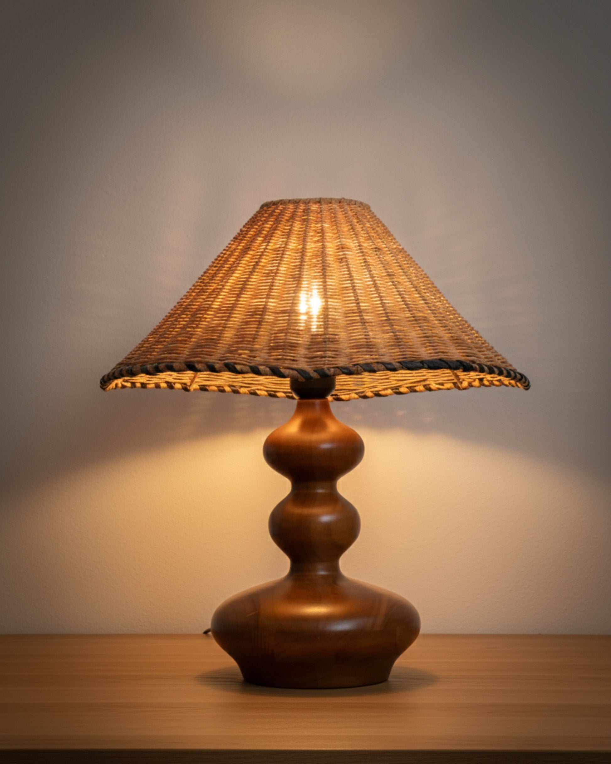 Handwoven rattan table lamp with sculpted ash-wood base (walnut tone), 400 mm (15.75") shade, 450 mm (17.72") tall, shown lit on a bedside table; soft ambient glow for Japandi/Scandinavian interiors.