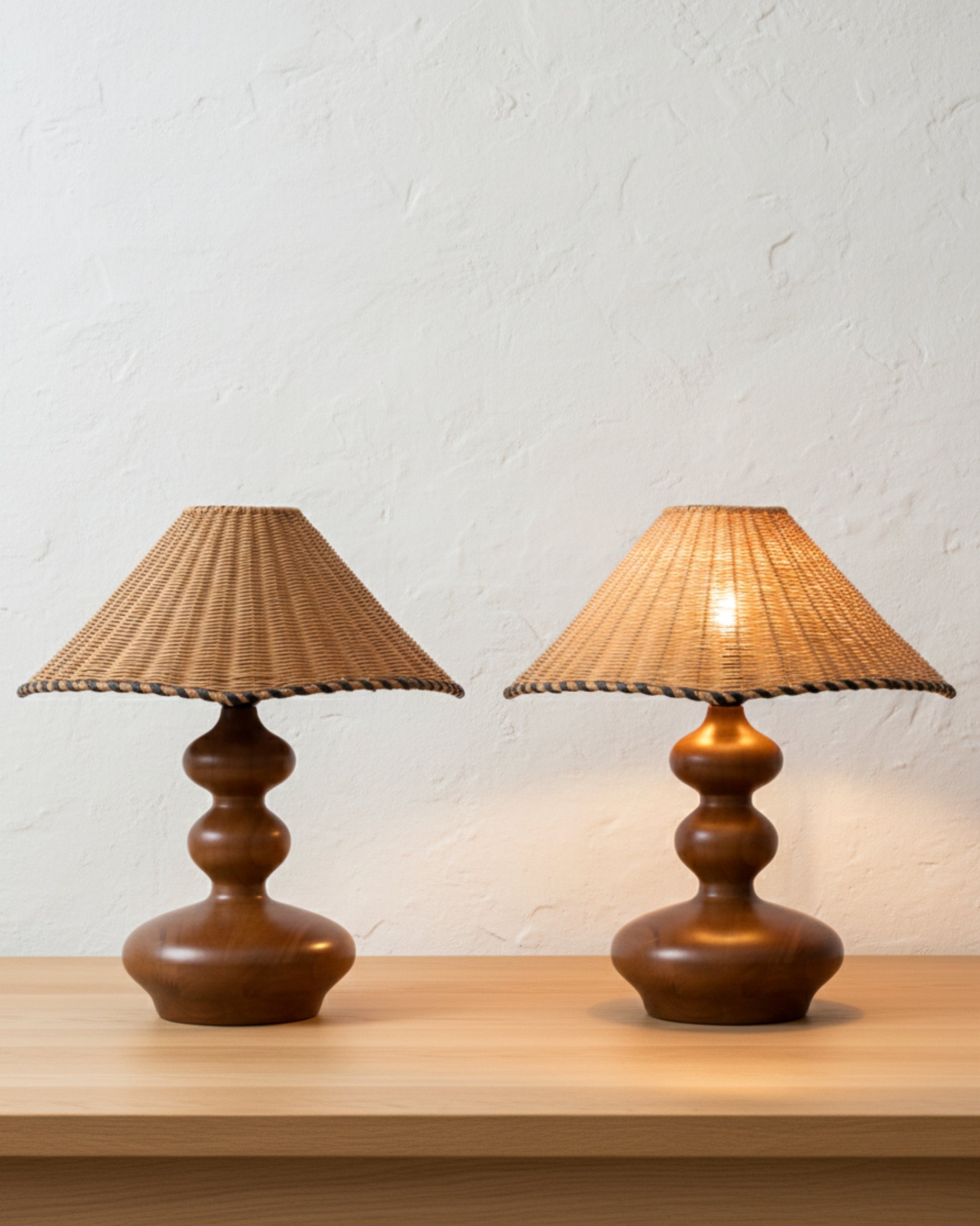 Two handwoven rattan table lamps with sculpted ash-wood bases (walnut tone), 40 cm (15.75") conical shades on a light wood surface; left lamp off, right lamp lit with a warm 2700K glow against a textured plaster wall.