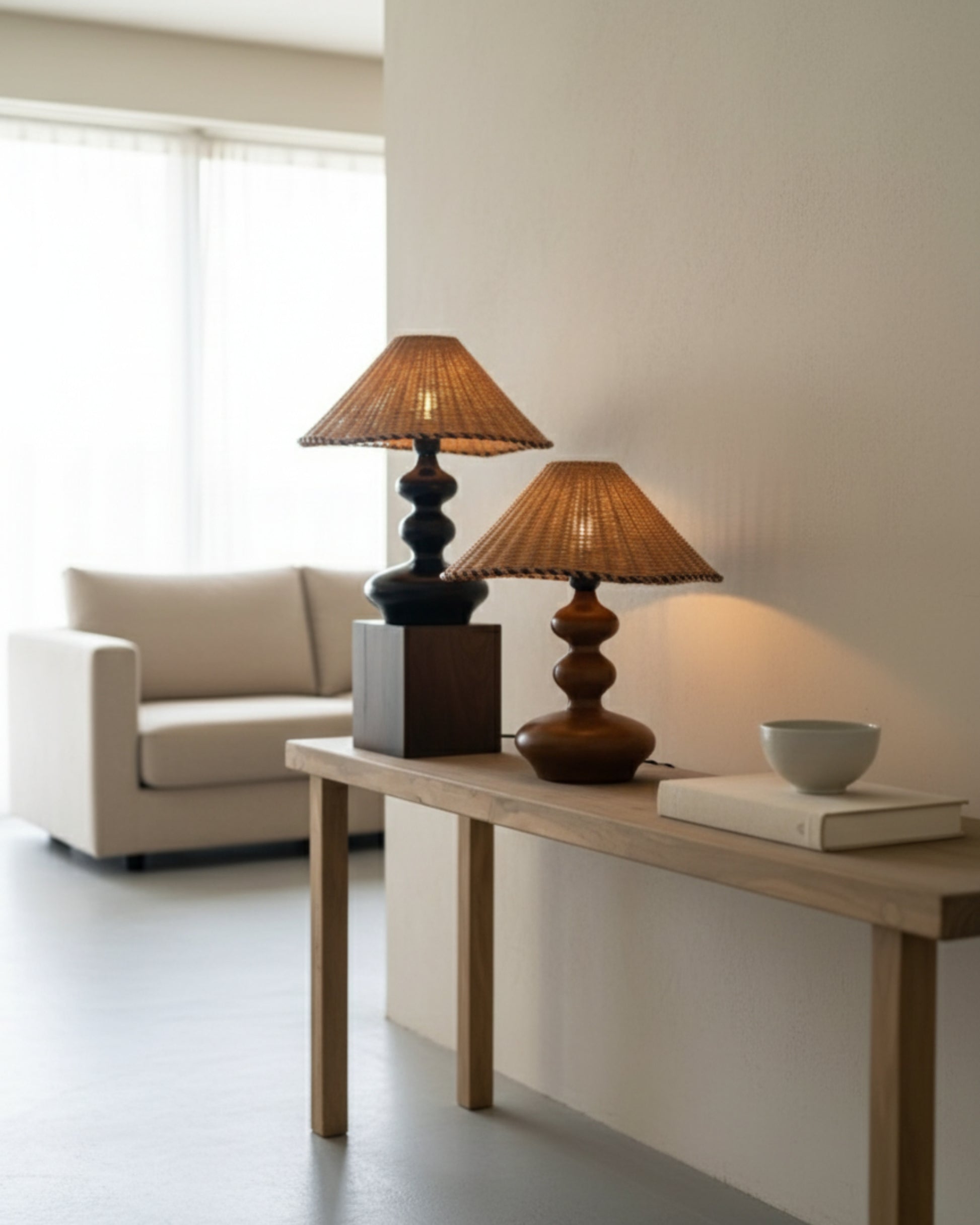 Two handwoven rattan table lamps with sculpted wood bases (walnut and espresso), 40 cm (15.75") conical shades, lit on a light wood console; soft ambient glow in a minimalist Japandi living room.