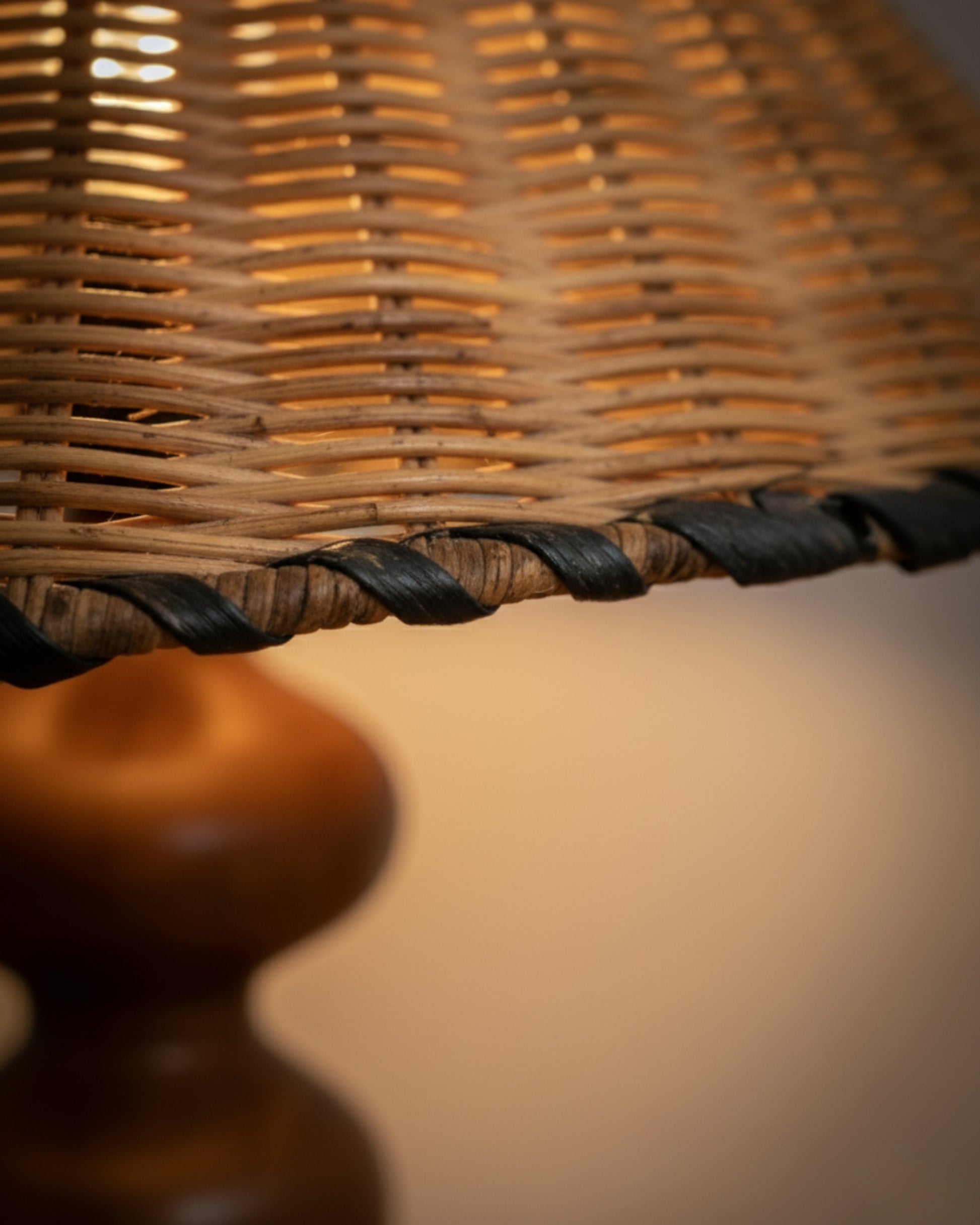 Close-up of the handwoven rattan shade with a braided black edge; warm 2700K light glows through the weave. Detail of the 40 cm (15.75") shade with the ash-wood base softly blurred in the background.